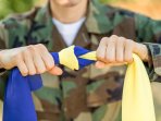 Юнак у військовій формі тримає зав'язаний прапор України