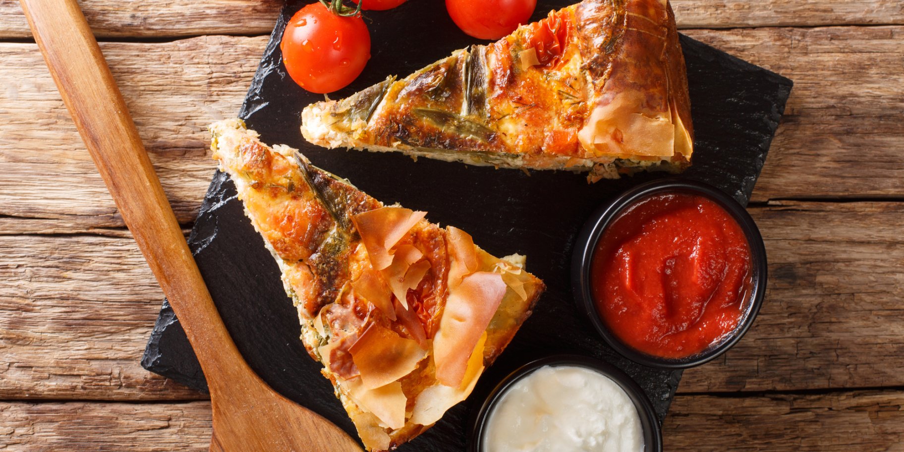 Два шматки пирога на чорній тарілці з помідорами