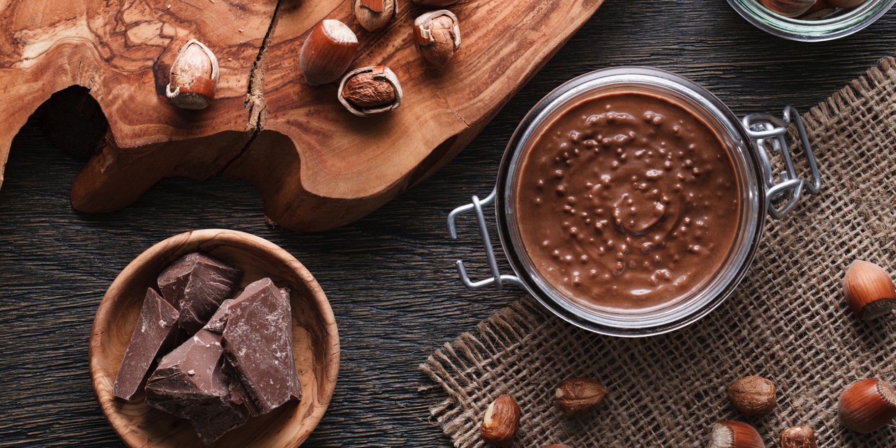 Шоколадный соус в банке рядом с шоколадом и орехами вокруг