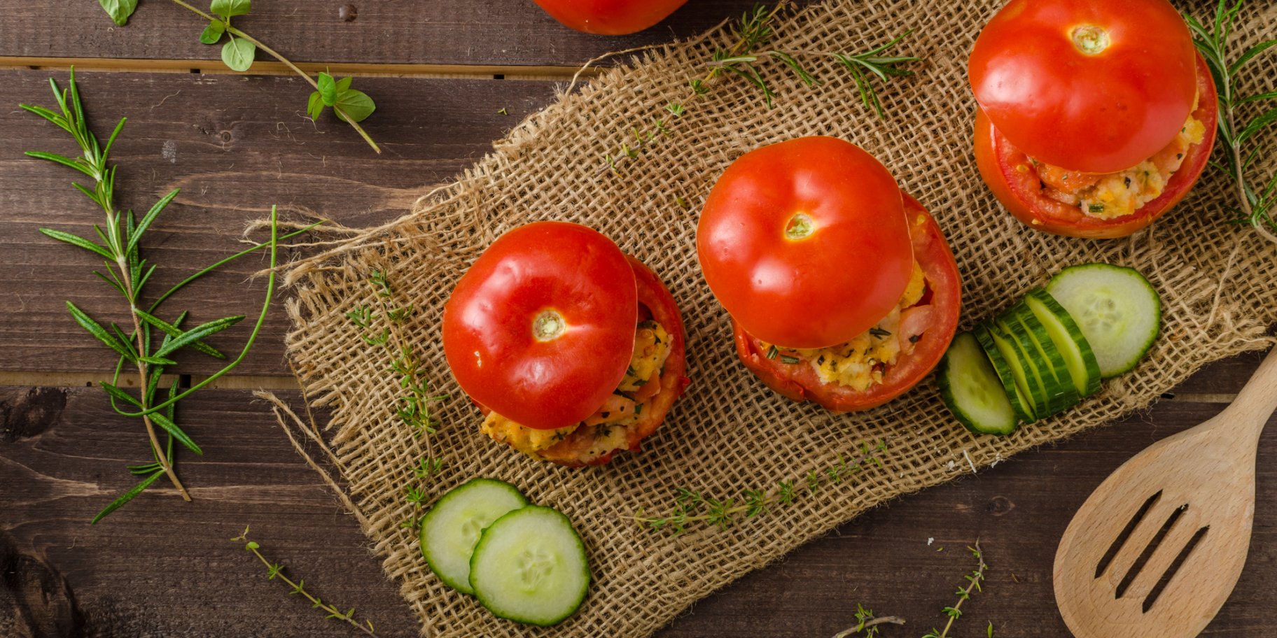 Три фаршированные начинкой помидора на салфетке с нарезанным огурцом на деревянном столе