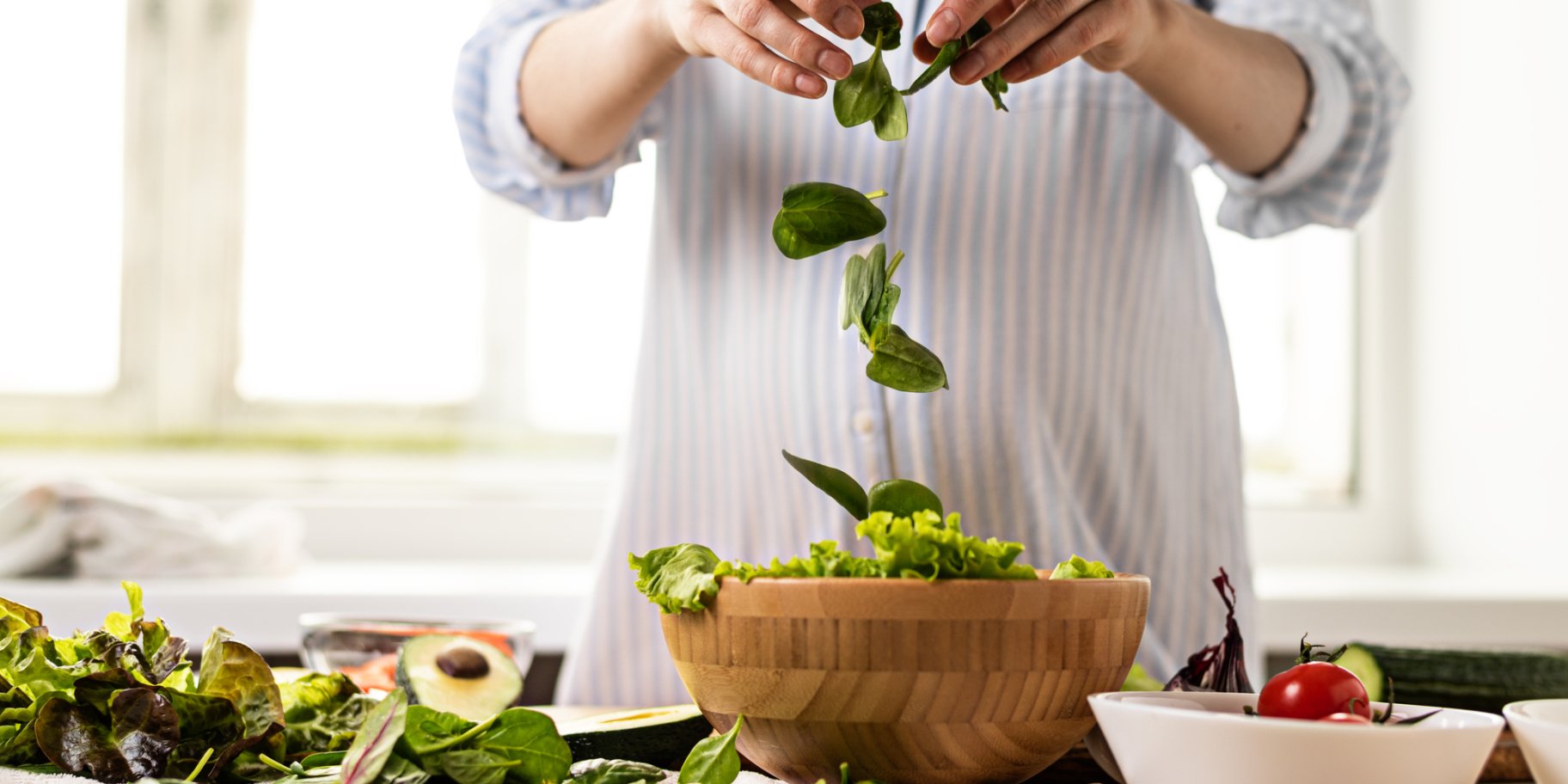Людина насипає в миску листя салату