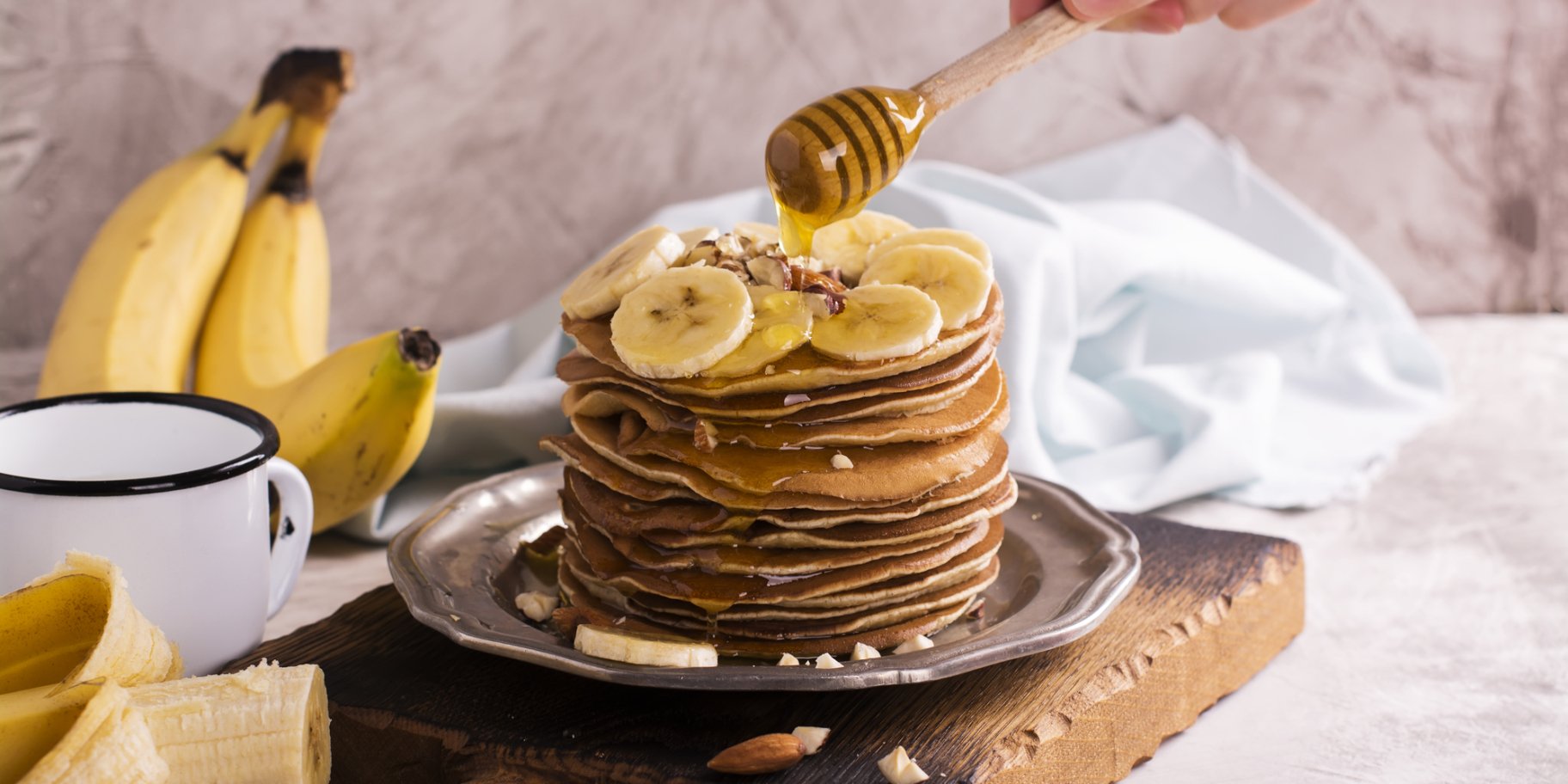 Панкейки з бананом та медом на коричневій дошці з білою чашкою поруч