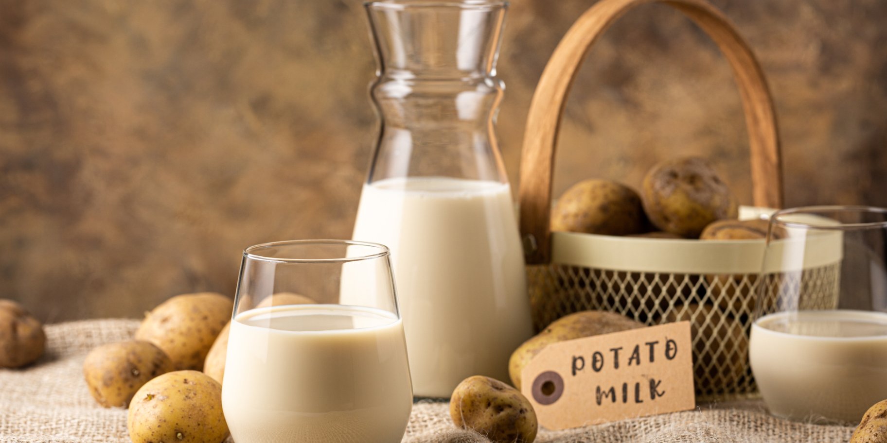 Склянка молока та пляшка на фоні кошика на скатертині поруч з картоплею