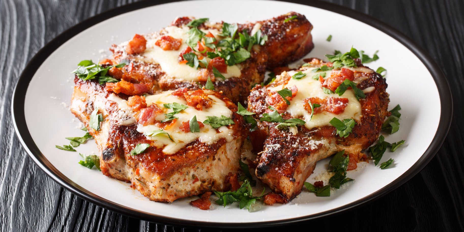 Три відбивні з сиром на білій тарілці на фоні дерев'яного столу