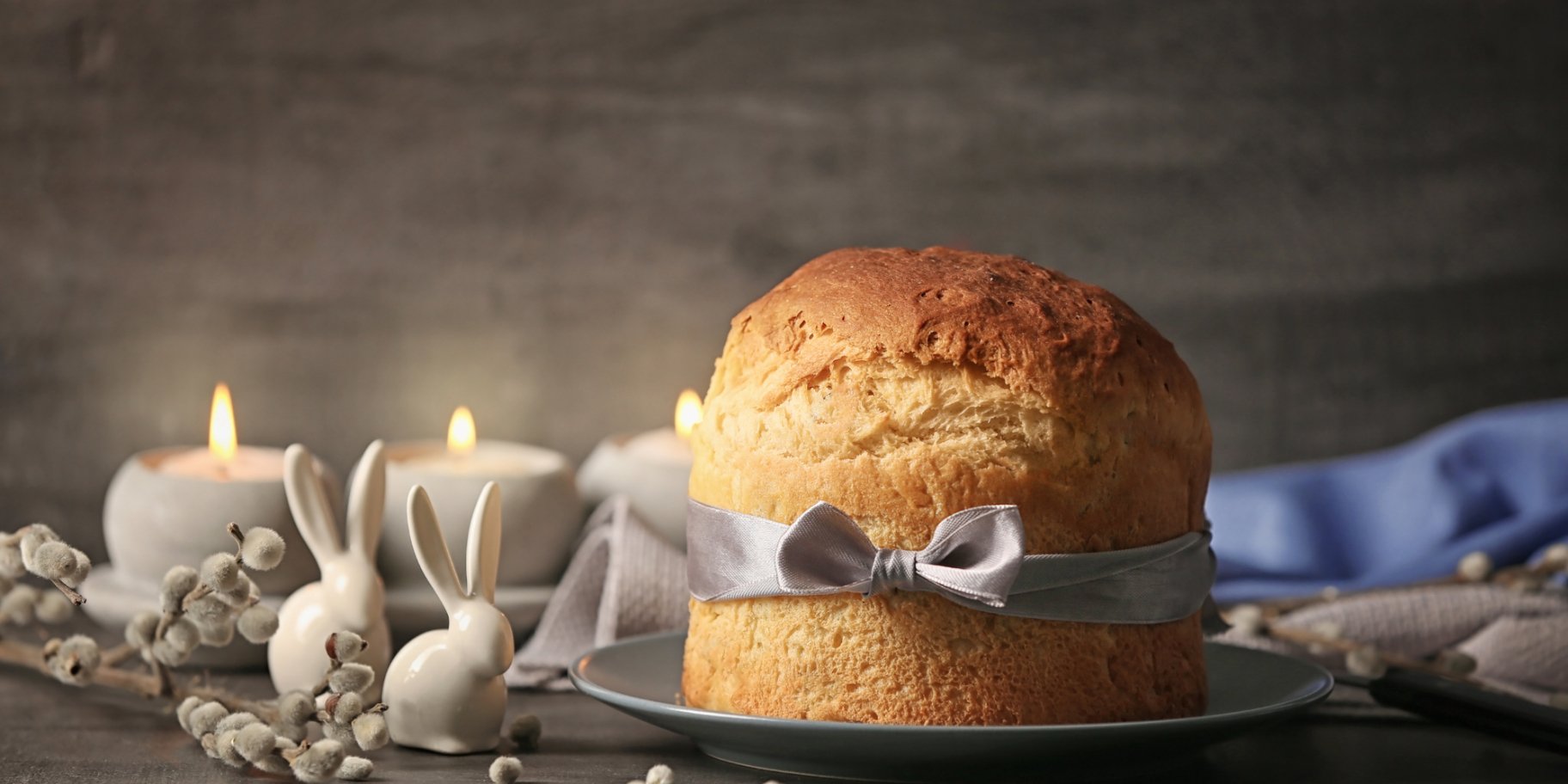 Паска, перев'язана стрічкою на темному фоні зі свічками та кроликами