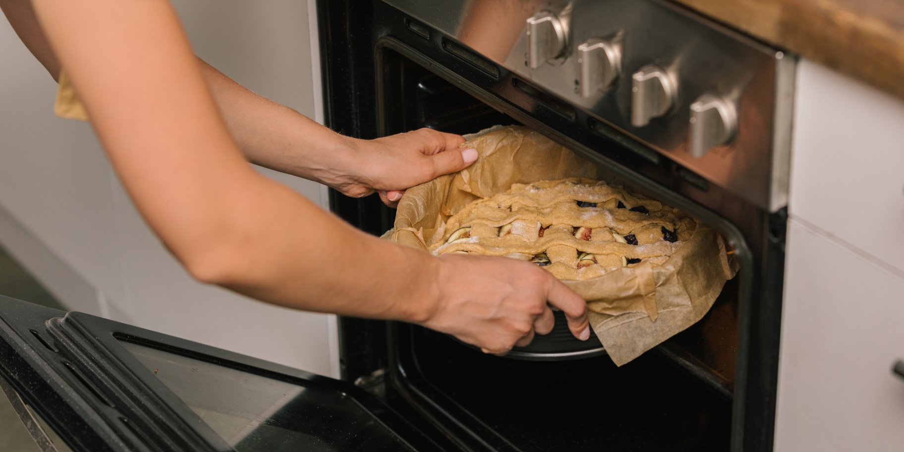 Женщина ставит в духовку пирог.
