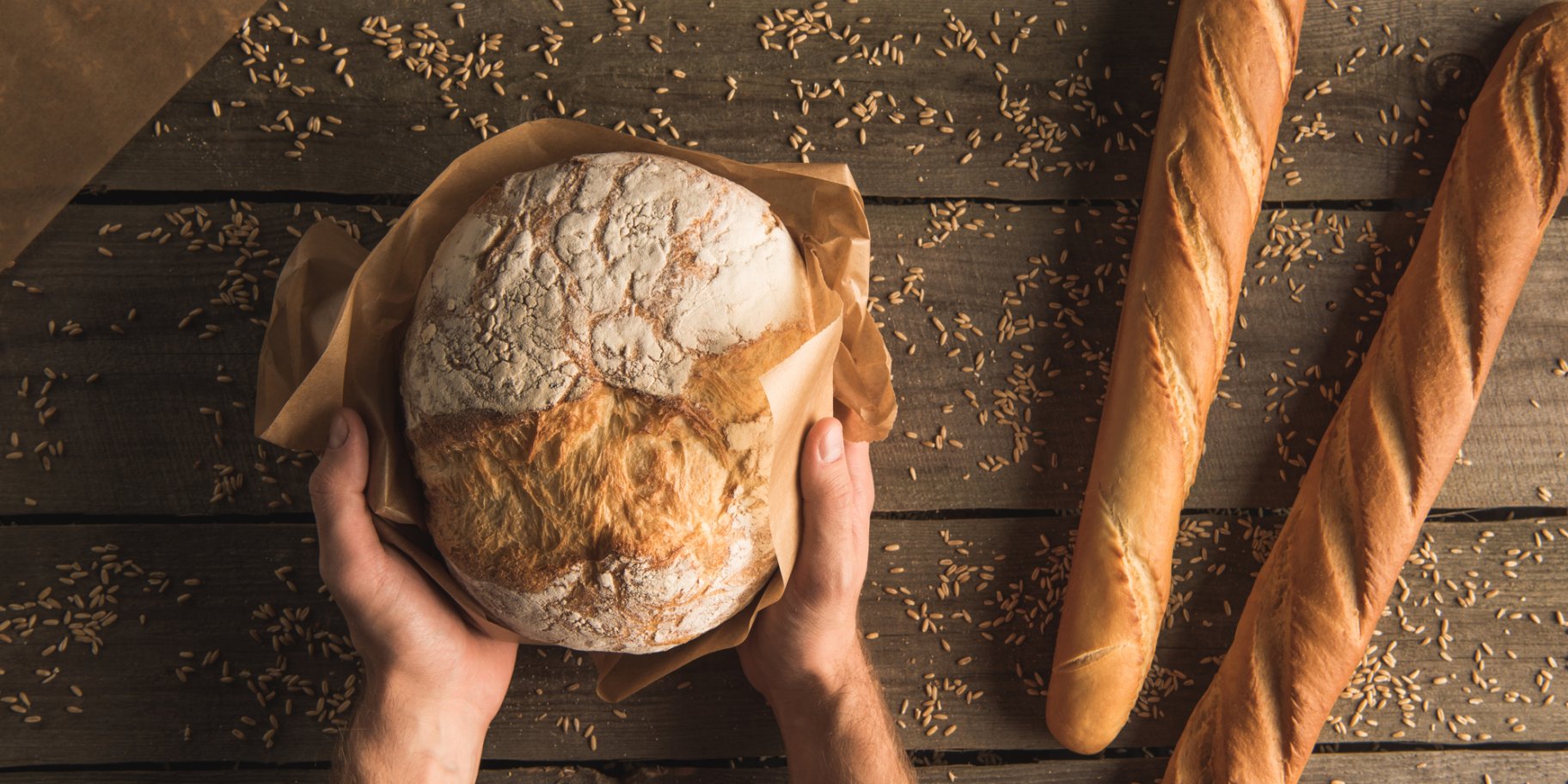 Хлеб и два багета с руками на фоне деревянного стола