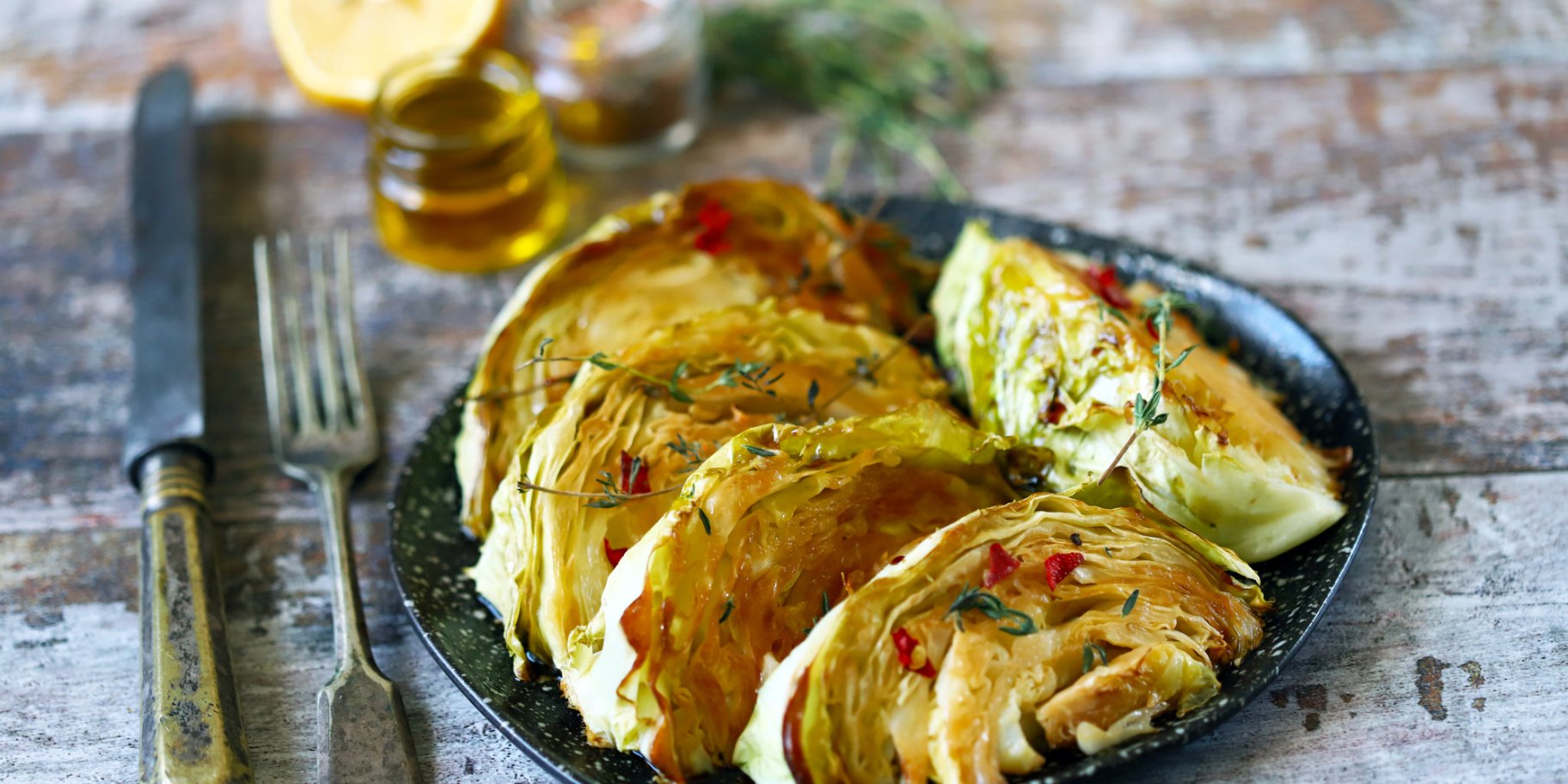 Печена дольками капуста в тарілці на фоні дерев'яного столу