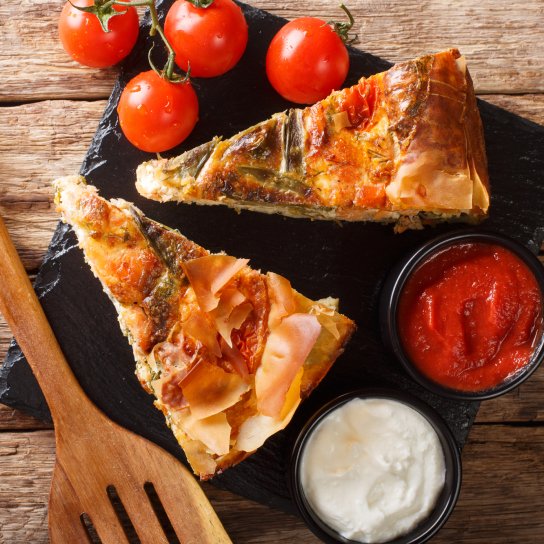 Два шматки пирога на чорній тарілці з помідорами