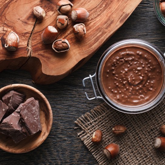 Шоколадний соус у банці поруч із шоколадом та горіхами навколо
