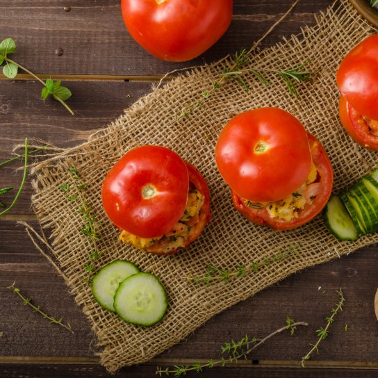 Три фаршировані начинкою помідори на серветці з нарізаним огірком на дерев'яному столі