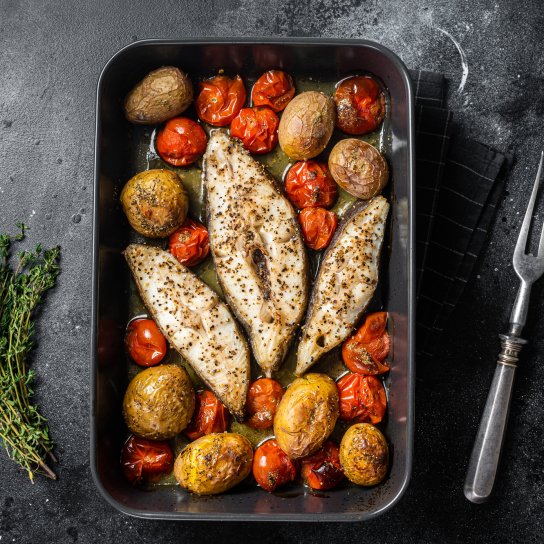 Три стейки палтуса, запечені з овочами, у чорній формі