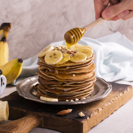 Панкейки з бананом та медом на коричневій дошці з білою чашкою поруч