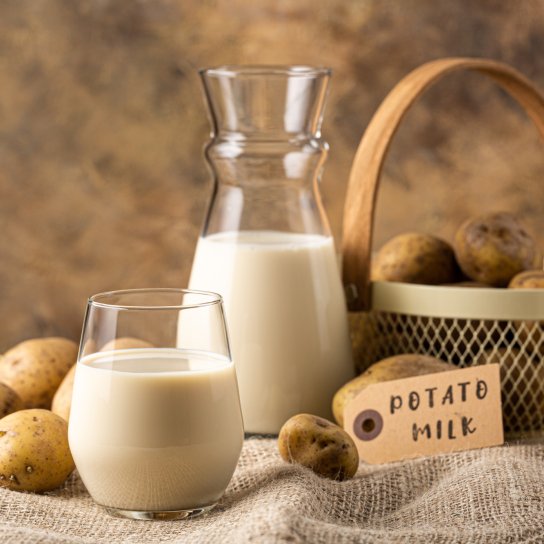 Стакан молока и бутылка на фоне корзины на скатерти рядом с картофелем