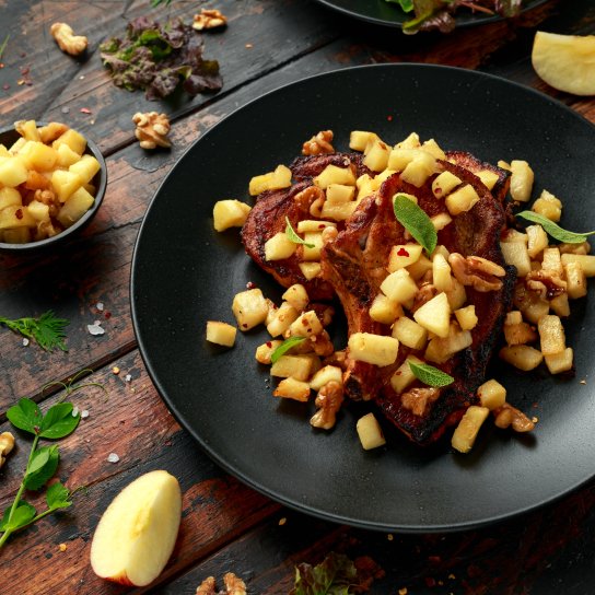 Свиняча відбивна з яблуками в чорній тарілці