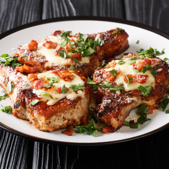 Три відбивні з сиром на білій тарілці на фоні дерев'яного столу