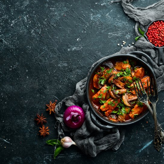 Форма для запікання з куркою в томатному соусі на фоні темного столу