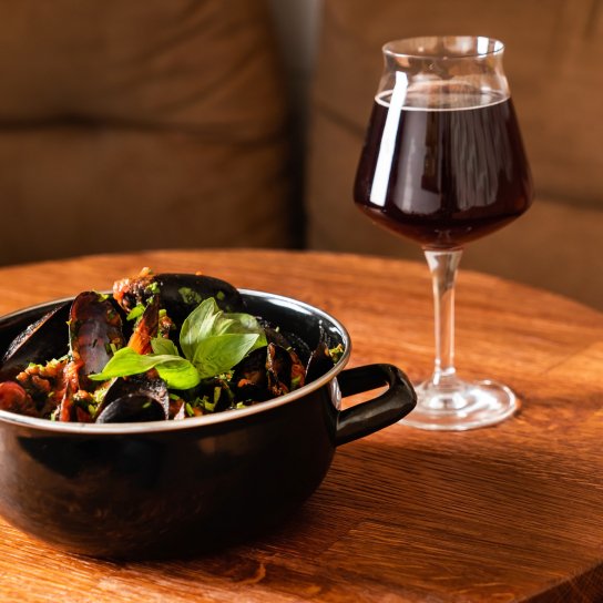 Каструля з мідіями та келих пива на дерев'яному столі