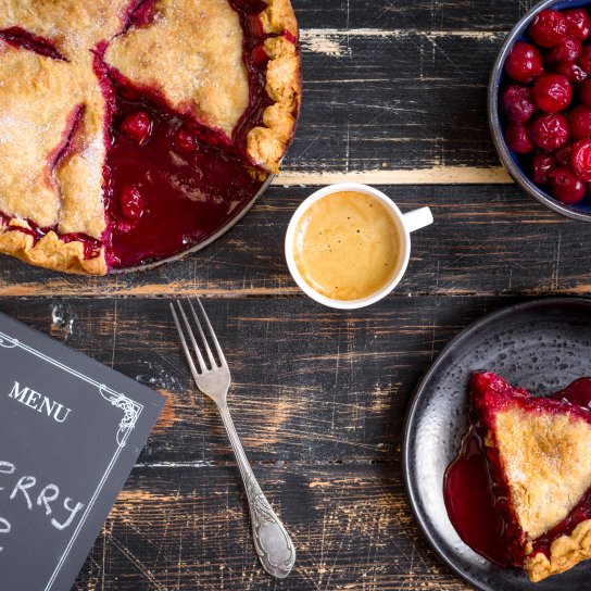 Вишневий пиріг, тарілка з вишнями, шматок вишневого пирога та чашка кави на дерев'яному столі
