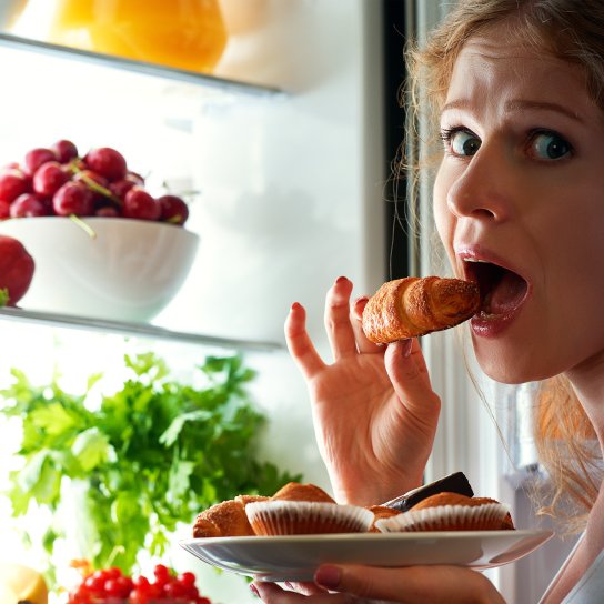 Жінка їсть круасан біля холодильника