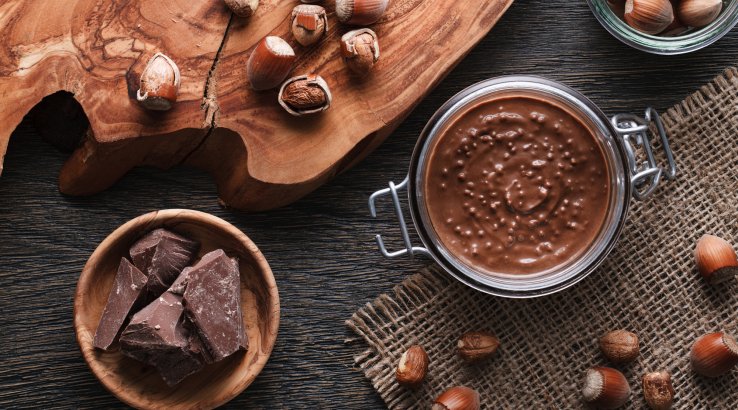 Шоколадний соус у банці поруч із шоколадом та горіхами навколо