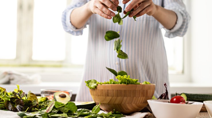 Человек насыпает в миску листья салата