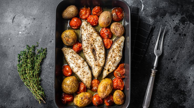 Три стейки палтуса, запечені з овочами, у чорній формі