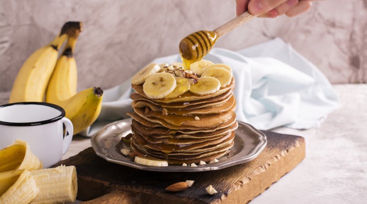 Панкейки з бананом та медом на коричневій дошці з білою чашкою поруч