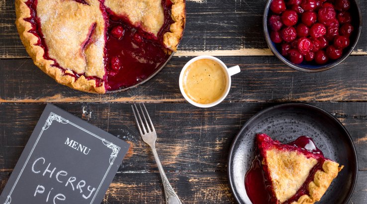 Вишневий пиріг, тарілка з вишнями, шматок вишневого пирога та чашка кави на дерев'яному столі