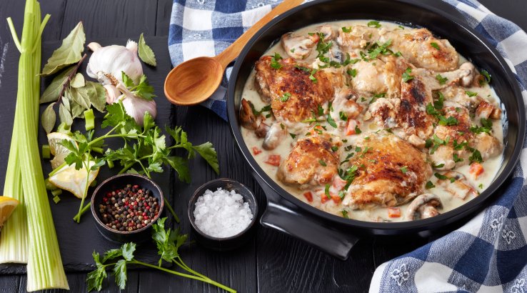 Курячі стегна у вершково-винному соусі в чорній тарілці з селерою та часником